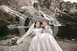 Beautiful wedding photosession. The groom circles his young bride, on the shore of the lake Morskie Oko. Poland