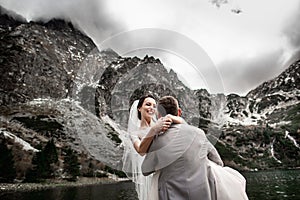 Beautiful wedding photosession. The groom circles his young bride, on the shore of the lake Morskie Oko. Poland