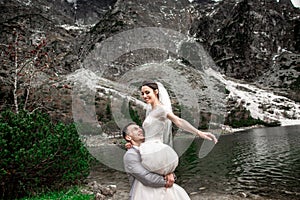 Beautiful wedding photosession. The groom circles his young bride, on the shore of the lake Morskie Oko. Poland