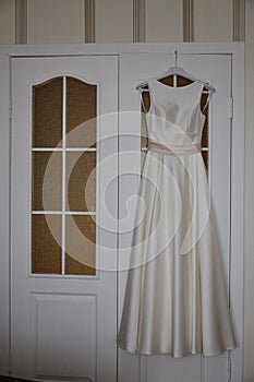 Beautiful wedding satin dress hanging on the door