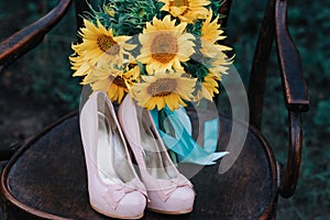 Beautiful wedding shoes with high heels and a bouquet of sunflowers on a vintage chair