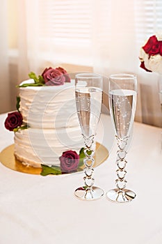 Beautiful white cake with red roses and two glasses with champagne