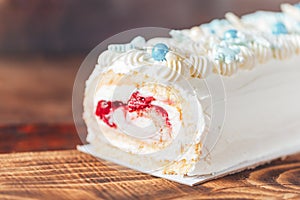 Beautiful white cake roll in front of a wooden background. The cake has snowflake-shaped confectionery decorations