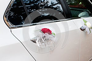Beautiful white car decorated with red flower boutonniere for the bride and groom on the wedding day