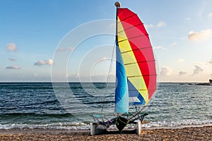 Beautiful white catamaran with red and yellow and blue sail and equipment is on the gold beach on the wet sand by turquoise sea on