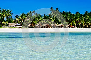 Beautiful white coral sand beach with palms and cottages, turquoise blue ocean