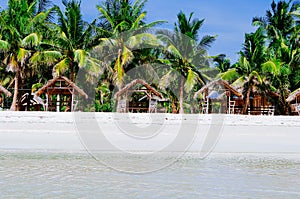 Beautiful white coral sand beach with palms and cottages, turquoise blue ocean