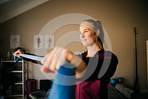 Beautiful white female physio stretching blue theraband while standing in studio.