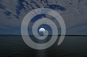 Beautiful white full moon and clouds in blue sky over the lake and mountains