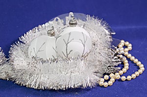 Beautiful white glass New Year`s balls with a silver pattern, white brilliant tinsel, cone and a pearl beads on a blue background