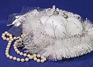 Beautiful white glass New Year`s balls with a silver pattern, white brilliant tinsel, cone and a pearl beads on a blue background