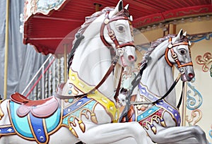 Beautiful white horses Christmas carousel in a holiday park. Two horses on a traditional fairground vintage Paris carousel. Merry-