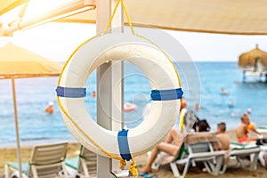 Beautiful white lifebuoy hanged on umbrella at tropical sandy beach. Life saver ring with beautiful blue sea coast on exotic