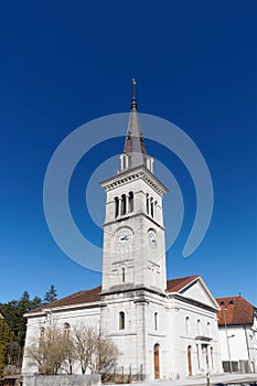 Beautiful white neoclassical style church with cock and bell tower against clear blue sky