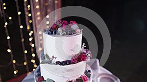 A beautiful white original handmade wedding cake stands in the lighting near the wedding arch in the evening. camera