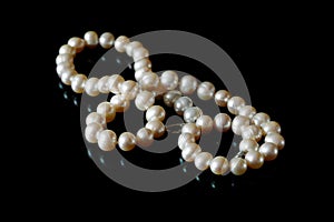 Beautiful white pearls necklace on black background, top view