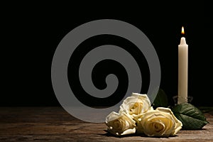 Beautiful white roses and candle on table against black background