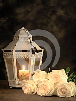 Beautiful white roses and candle on table against black background