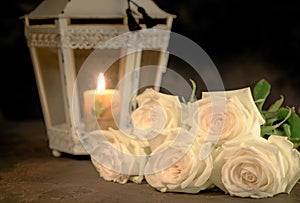 Beautiful white roses and candle on table against black background