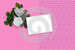 Beautiful white roses with green foliage and heart for Valentine`s Day on pink paper background. Creative greeting card