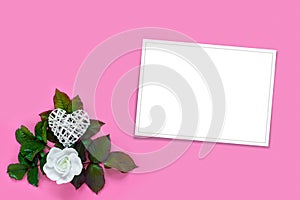 Beautiful white roses with green foliage and heart for Valentine\'s Day on pink paper background. Creative greeting card