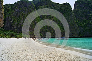 Beautiful white sandy beach beside the blue ocean surrounded by the treed rocks. Thailand.