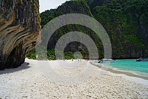 Beautiful white sandy beach beside the blue ocean surrounded by the treed rocks. Thailand.