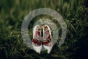 Beautiful white shoes with red bouquets on green grass close up