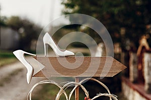 beautiful white shoes on wooden arrow with space for text. rustic wedding concept. pointing for wedding ceremony location.