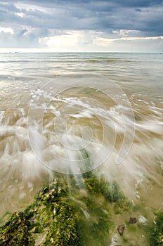 beautiful white and soft wave flow over the rock and mossy hitting the shore.dramatic dark clouds background before storm
