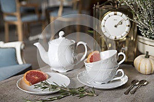 Beautiful white teapot, cups and saucer, antique clock, pumpkin, heather, rosemary and grapefruit. Still life.