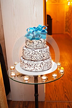 Beautiful white three-tier cake with a turquoise bow on top is on the table