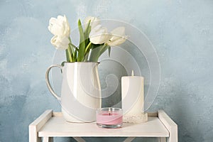 Beautiful white tulips and burning candles on wooden table against light blue background