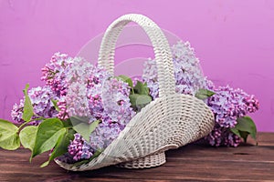 Beautiful white vintage wicker basket on a wooden table. Lilac flowers in a retro basket