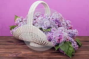 Beautiful white vintage wicker basket on a wooden table. Lilac flowers in a retro basket