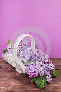 Beautiful white vintage wicker basket on a wooden table. Lilac flowers in a retro basket