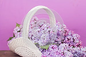 Beautiful white vintage wicker basket on a wooden table. Lilac flowers in a retro basket