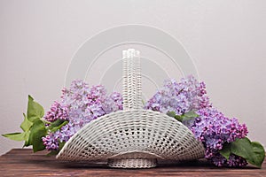 Beautiful white vintage wicker basket on a wooden table. Lilac flowers in a retro basket