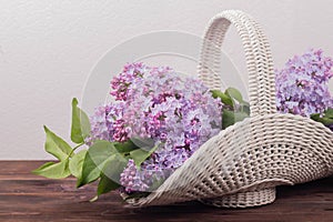 Beautiful white vintage wicker basket on a wooden table. Lilac flowers in a retro basket