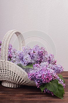 Beautiful white vintage wicker basket on a wooden table. Lilac flowers in a retro basket