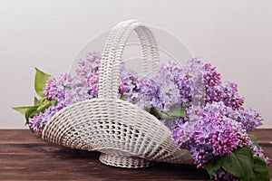 Beautiful white vintage wicker basket on a wooden table. Lilac flowers in a retro basket