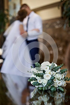 Beautiful white wedding bridal bouquet and on the background kiss the bride and groom