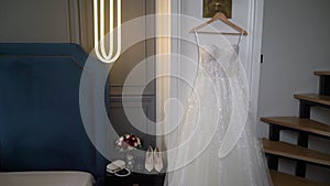 Beautiful white wedding dress hangs on a hanger in the bedroom.