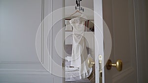 Beautiful white wedding dress hangs on a hanger in the bedroom.