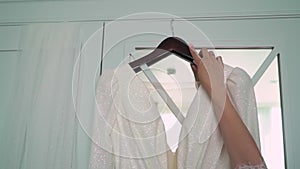 Beautiful white wedding dress hangs on a hanger on the wardrobe in the bedroom.