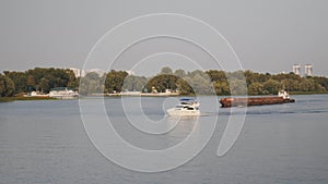 Beautiful white yacht floating on river. Small white boat and old rusty barge sail on river.