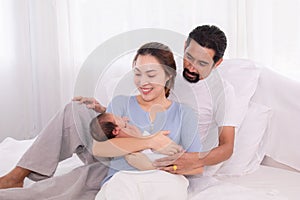 Beautiful wife leaning her back to husband leg while hold newborn with love and carefully, happy Hispanic father with beard or mix