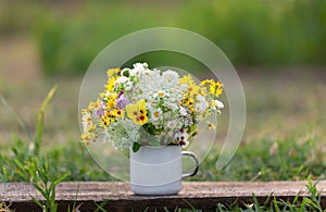 Beautiful wild flowers in white cup on wooden table and nature background