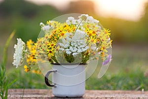 Beautiful wild flowers in white cup on wooden table and nature background