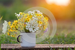 Beautiful wild flowers in white cup on wooden table and nature background